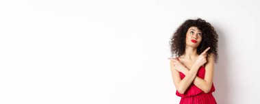 Kırmızı elbiseli, çapraz parmaklı, yana bakan, dalgın dalgın bakan, seçim yapan, beyaz arka planda duran kararsız budala kadın..