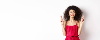 Umutlu, kıvırcık saçlı, şans dileyen, gülümseyen, dilek tutan, dua eden, beyaz arka planda duran güzel kız..