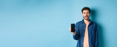 Mutlu beyaz adam boş bir ekran gösteriyor ve gülümsüyor, mavi arka planda duruyor..