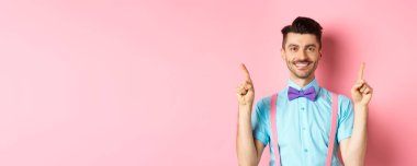 Neşeli yakışıklı adam kameraya gülümsüyor, parmaklarını havaya kaldırıyor, pembe arka planda reklam yapıyor..