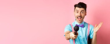 Neşeli genç adam, papyonlu sunucu sana mikrofon veriyor ve gülümsüyor, bayramlarda insanları eğlendiriyor, pembe arka planda duruyor..