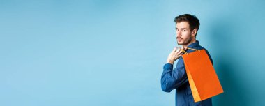 Arkaya bakan mutlu adam arkasını kolluyor ve mavi arka planda duruyor..