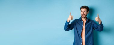 Yakışıklı genç adam boş alana bakıyor ve mavi arka planda dikiliyor..