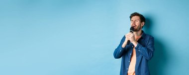 Romantik adam mikrofonda şarkı söylüyor, sahnede şarkı söylüyor, mavi arka planda duruyor..