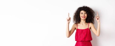 Zarif kırmızı elbiseli ve makyajlı, gülümseyen kadın, sevgililer gününde, beyaz arka planda duran ve tanıtım teklifini gösteren..