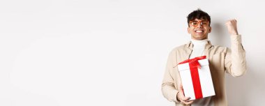 Neşeli adam hediye olarak evet diyor, yumruk tokuşturuyor ve seviniyor, beyaz arka planda duruyor..