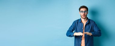 Gözlükçüde güneş gözlüğü deneyen, dans eden ve eğlenen, mavi arka planda duran komik adam..