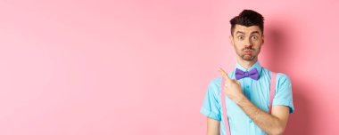 Etkileyici bir teklif sunan genç adam, kaşlarını kaldırıyor ve ilgili görünüyor, sol üst köşeyi işaret ediyor, pembe arka plan..