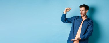 Büyük bir nesneyle boş alana bakan, büyük boyutlarda, mavi arka planda duran, etkileyici bir beyaz adam..