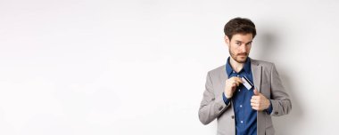 Kendine güveni tam ve başarılı bir iş adamı gibi görünen ve beyaz arka planda duran plastik kredi kartını takım elbisenin cebine koyan..