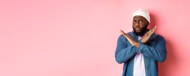 Hayal kırıklığına uğramış siyah adam, kameraya kızgın ve somurtkan bakıyor, dur işareti yapıyor, yasaklıyor ve katılmıyor, pembe arka planda duruyor..