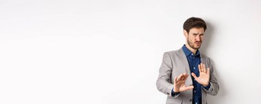 Uzak dur benden. İsteksiz işadamı endişeli bir yüz ifadesiyle geri adım atar, kötü teklifi engellemek için ellerini kaldırır, korkunç bir şeyi reddeder, hayır der ve teklifi reddeder, beyaz arka plan.