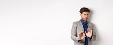 Uzak dur benden. İsteksiz işadamı endişeli bir yüz ifadesiyle geri adım atar, kötü teklifi engellemek için ellerini kaldırır, korkunç bir şeyi reddeder, hayır der ve teklifi reddeder, beyaz arka plan.