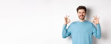 - Çok iyi. Gülümseyen yakışıklı iyi işaretler gösteriyor ve tatmin olmuş görünüyor, beyaz arka planda duruyor, mükemmel bir seçimi onaylıyor..