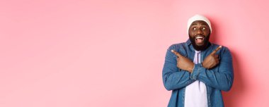 Heyecanlı genç Afro-Amerikalı adam iki seçenek gösteriyor ve karar veriyor, mutlu bir şekilde gülümsüyor, pembe arka planda duruyor..