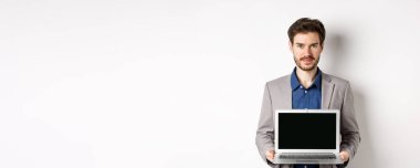 Takım elbiseli yakışıklı beyaz işadamı boş laptop ekranı gösteriyor, tanıtım yapıyor, beyaz arka planda duruyor..