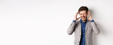 Hayal kırıklığına uğramış takım elbiseli bir iş adamı çıldırıyor, çığlık atıyor ve kafasının yanında el sıkışıyor, sinirli ya da sinirli hissediyor, sıkıntılı bağırıyor, beyaz arka planda duruyor..