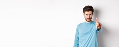 Sakallı, parmağını sallayarak onaylamadığı, bir şeyi yasakladığı ya da yasakladığı beyaz arka planda duran ve hayır diyen ciddi bir gencin görüntüsü..