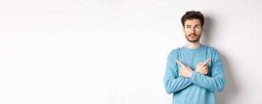 Kararsız adam seçim yapıyor, parmaklarını iki varyanta doğrultuyor ve karar veriyor, sol tarafta dalgın dalgın bakıyor, beyaz arka planda duruyor..