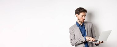 Heyecanlı satıcı dizüstü bilgisayar ekranına bakıyor şaşkın, heyecandan uzak duruyor, ağdaki haberleri kontrol ediyor, beyaz arka planda duruyor..