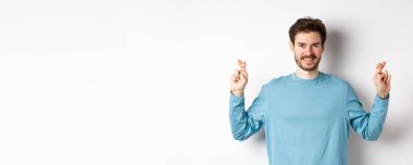 İyimser gülümseyen adam şans diliyor, dilek diliyor ve sonuçları bekliyor, beyaz arka planda duruyor..