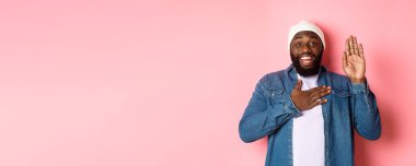 Gülümseyen Afro-Amerikan bir adamın dürüst olması, doğruyu söylemesi, ellerini havaya kaldırması, söz vermesi ya da küfretmesi, pembe arka planda durması..