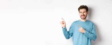 Mavi kazaklı genç bir adamın portresi sol üst köşeyi işaret ediyor ve yüzünü çeviriyor. Beyaz arka planda reklamını yaparken mutlu bir şekilde gülümsüyor..