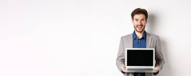 Takım elbiseli yakışıklı beyaz işadamı boş laptop ekranı gösteriyor, tanıtım yapıyor, beyaz arka planda duruyor..