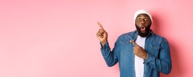 Harika bir tanıtım teklifi sunan siyahi adam, kameraya bakıyor, heyecanlı ve gülümsüyor, sol üst köşedeki afişi işaret ediyor, pembe arka plan..
