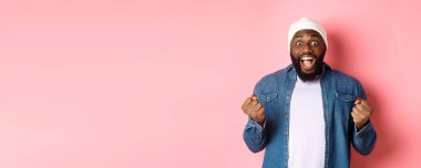 Şaşırmış ve mutlu adam kazanırken inançsızlıkla bakıyor, yumruklarını sıkıyor ve gülümsüyor şaşkınlıkla, zaferi kutluyor, amacına ulaşıyor, pembe arka planda duruyor..