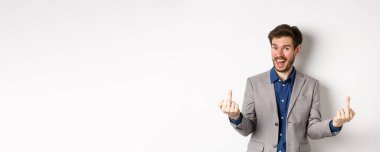 Rude ignorant guy in business suit showing middle fingers and tongue, smiling while mocking people, fuck you gesture, standing on white background.