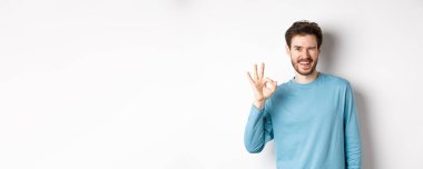 Yakışıklı, kendine güvenen, tamam işareti gösteren ve sana göz kırpan, her şeyin yolunda olduğuna emin olan, beyaz arka planda duran,.