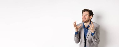 İş adamı kılığındaki kızgın adam nefretle sol tarafa bakar, kenarda durup dişlerini sıkmış el sıkışır, kızgın ve öfkeli durur, beyaz arka planda birini öldürmek ister..