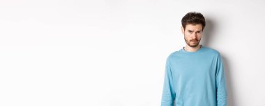 Üzgün genç sakallı adam, kameraya üzgün bakıyor, biri tarafından rahatsız ediliyor, beyaz arka plana karşı duruyor..