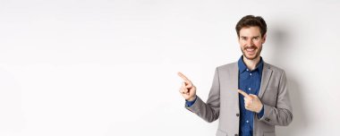 Beyaz takım elbiseli yakışıklı beyaz adam sol pankartı işaret ediyor ve gülümsüyor, reklam yapıyor, beyaz arka plana karşı duruyor..