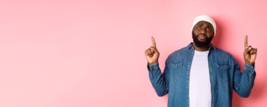 Üzgün ve kasvetli, bereli Afro-Amerikan adam, parmaklarını havaya kaldırıyor, iç çekiyor ve üzüntü ile en üste bakıyor, pembe arka planda duruyor..