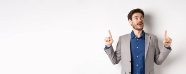 Heyecanlı, sakallı, takım elbiseli, neşeli görünüşlü, hayranlıkla tepede duran, beyaz arka planda duran yakışıklı adam..