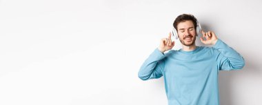 Kablosuz kulaklıkla müzik dinleyen yakışıklı bir adam ve gülümseyen, iyi sesin tadını çıkaran, beyaz arka plan.