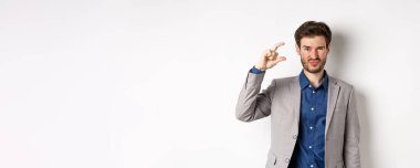 Hayal kırıklığına uğramış işadamı, küçük boyutlarda ve buruşuk suratlı üzgün, az gelirli, beyaz arka planda hoşnutsuz duruyor..