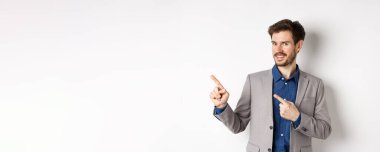 Gri takım elbiseli yakışıklı iş adamı logoyu işaret ediyor, reklamlara davet ediyor, beyaz arka planda duruyor..