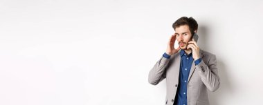 İş adamı telefonla konuşuyor ve kulaklarını kapatıyor, yüksek sesle çağrı alıyor, arayanı duymuyor, beyaz arka planda duruyor..