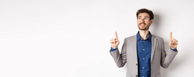 Takım elbiseli, gülümseyen, gülümseyen bir erkek yönetici, mutlu bir yüz, reklamlara bakıyor, beyaz arka planda duruyor..