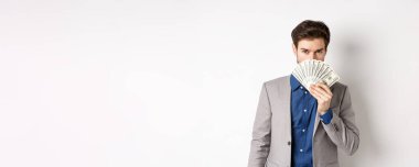 Takım elbiseli zengin bir işadamı. Para arkasında saklanıyor. Şehvetli bakışlarıyla kameraya bakıyor..