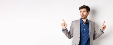 Karmaşık işadamı iki yolu işaret ediyor, seçmekte zorlanıyor, kenara bakıyor ve düşünüyor, karar veriyor, takım elbise içinde beyaz arka planda duruyor..