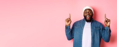 Neşeli siyahi adam harika bir reklam sunuyor, parmaklarını havaya kaldırıyor ve gülümsüyor, pembe arka planda duruyor..
