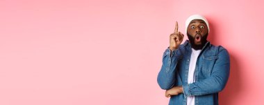 Yakışıklı hippi siyahi adamın bir fikri var, parmağını kaldırıp öneride bulunuyor, çözümü var, pembe arka planda duruyor..