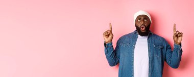 Hayal kırıklığına uğramış Afrikalı Amerikalı adam şikayet ediyor, kötü tanıtıma bakıyor ve işaret ediyor, pembe arka plana karşı hoşnutsuz duruyor..