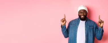 Yüzsüz Afrikalı Amerikalı adam gülümsüyor ve göz kırpıyor. Anlaşmayı üstte gösteriyor. Parmakla işaret ediyor, pembe arka planda duruyor..