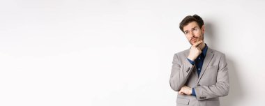 Gri takım elbiseli düşünceli bir işadamı sol üst köşedeki logoya bakar, düşünür ya da karar verir, plan yapar, beyaz arka plana karşı durur..