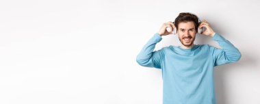 Adam müzik ya da podcast dinlemek için kablosuz kulaklık takmış, kameraya gülümsüyor, pembe arka planda duruyor..